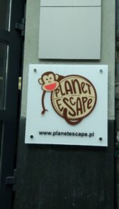 Tabliczka reklamowa z logiem firmy zamontowana przy wejściu do budynku.